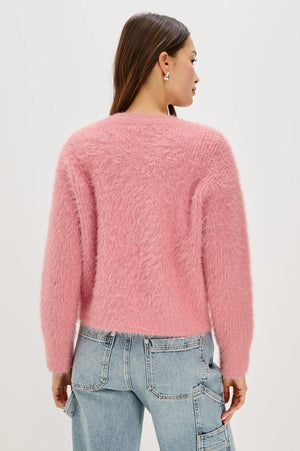 Person wearing a pink fuzzy sweater and blue jeans on a white background