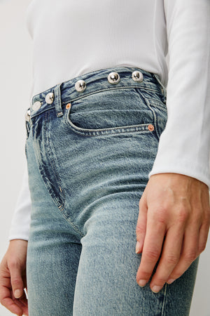 Close-up of light blue jeans with decorative buttons worn by a person.