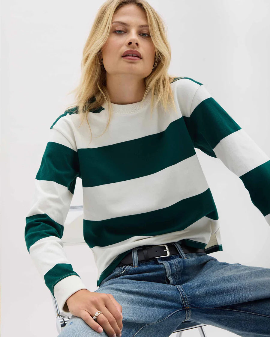 Woman wearing a green and white striped sweater with blue jeans on a light background