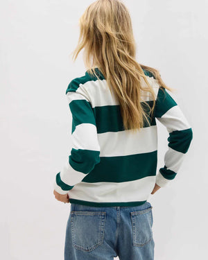 Person wearing a green and white striped sweater with blue jeans on a plain background
