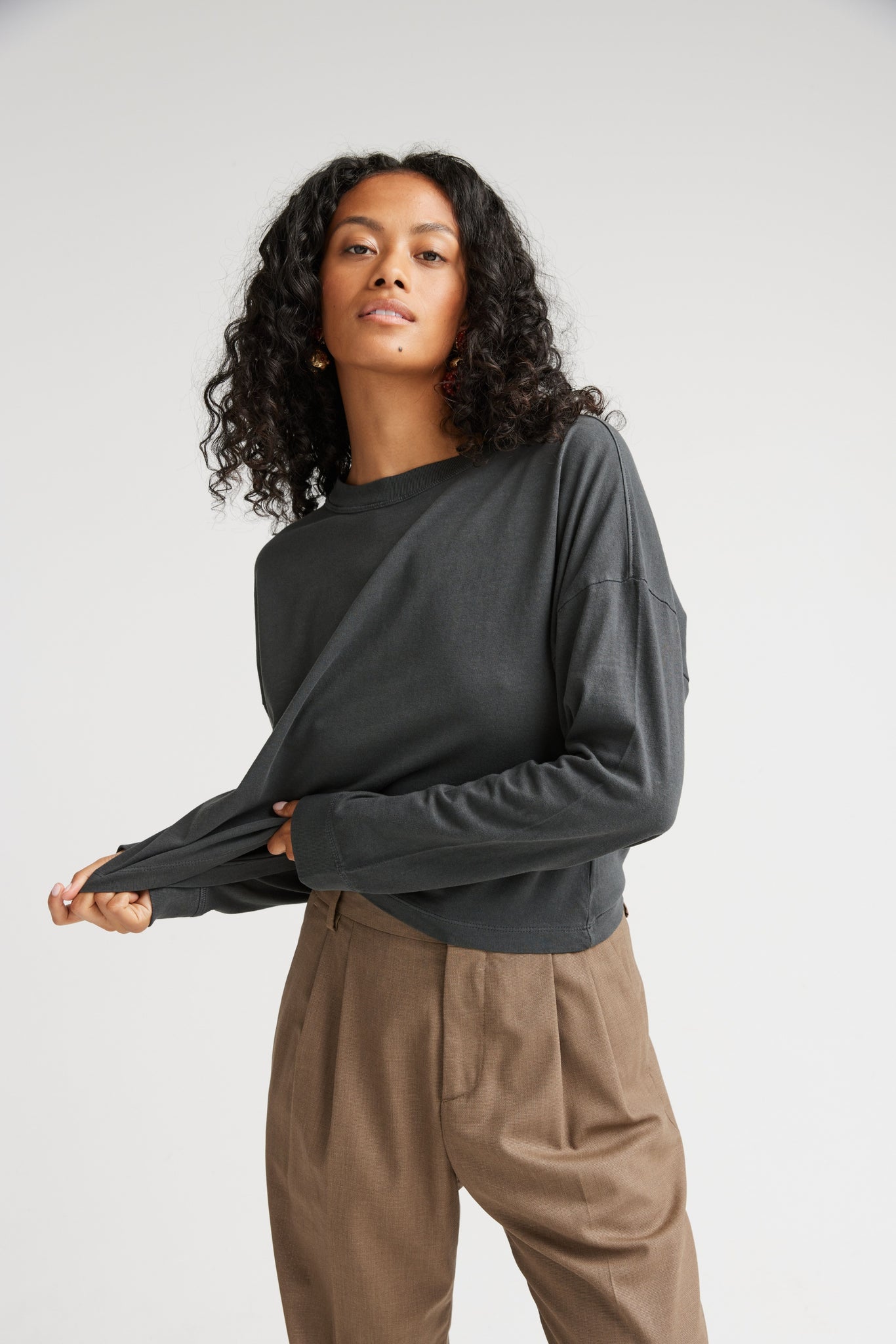 Woman wearing a dark green long-sleeve top and beige pants against a white background
