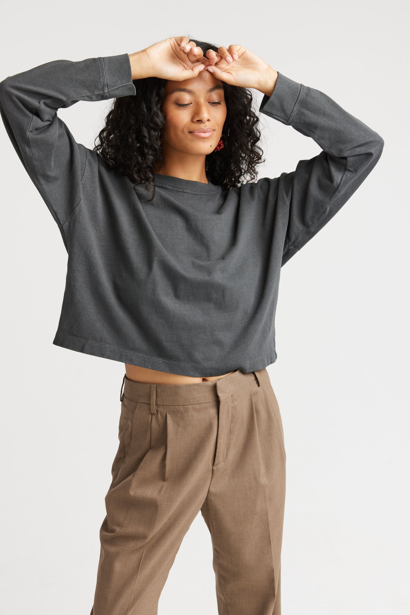 Person wearing a dark gray long-sleeve top and brown pants on a white background