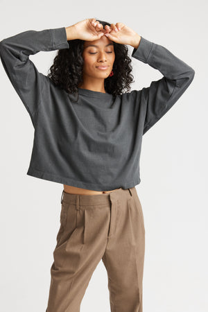Person wearing a dark gray long-sleeve top and brown pants on a white background