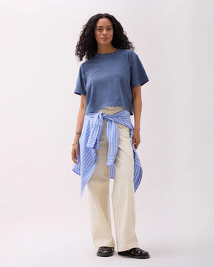 Woman wearing a blue top and beige pants with a striped shirt tied around her waist on a white background
