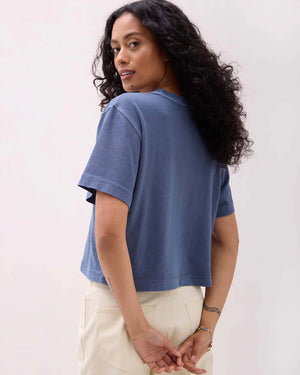 Woman wearing a blue t-shirt and white pants against a plain background