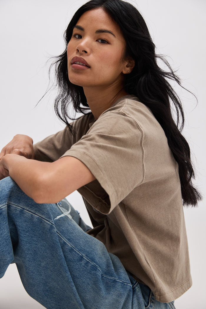 Woman wearing a beige t-shirt and blue jeans against a white background