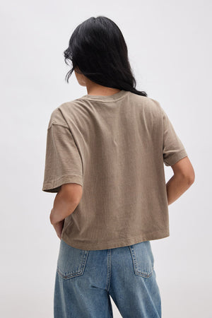 Person wearing a brown t-shirt and blue jeans on a white background