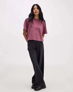 Woman wearing a mauve t-shirt and black pants on a white background