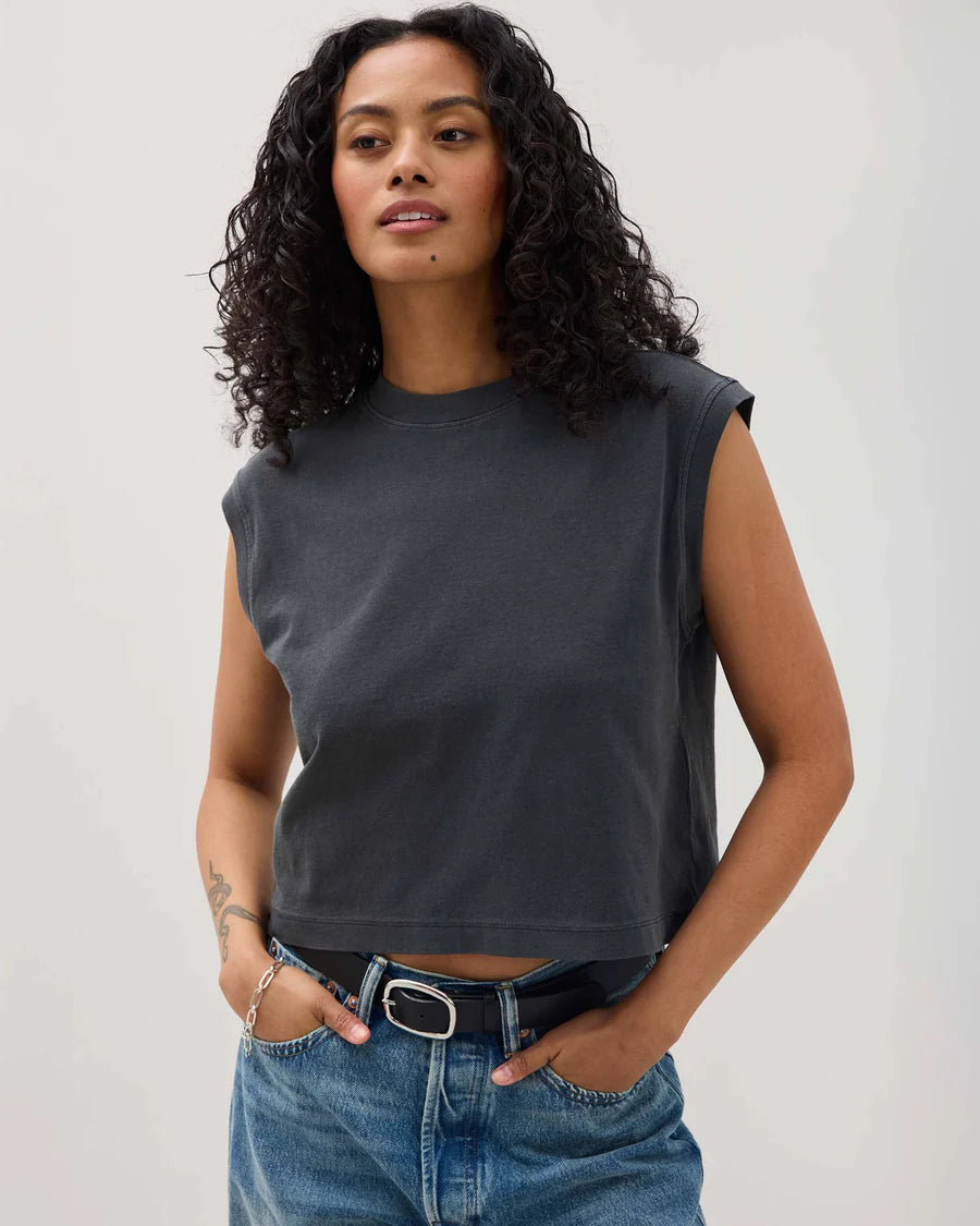 Woman wearing a dark gray sleeveless top and blue jeans against a plain background