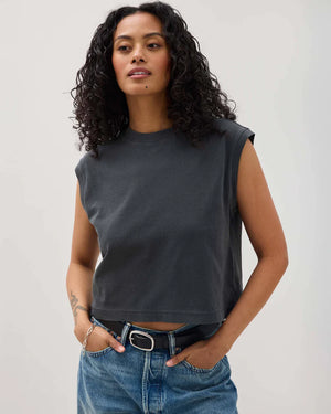 Woman wearing a dark gray sleeveless top and blue jeans against a plain background