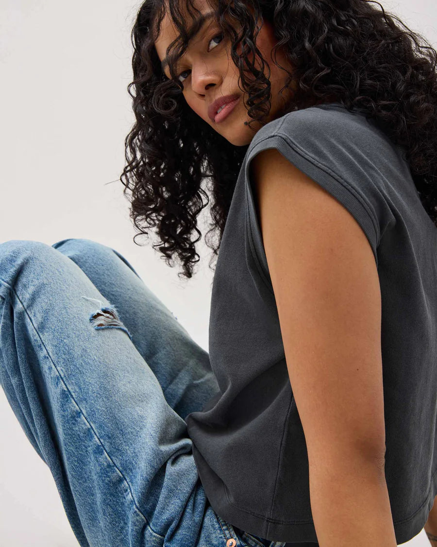Person wearing a sleeveless top and jeans against a plain background