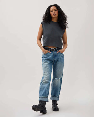 Woman wearing a sleeveless black top and blue jeans on a white background