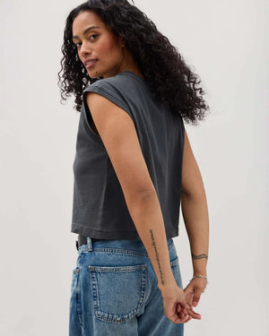 Woman wearing a dark gray sleeveless top and blue jeans against a plain background