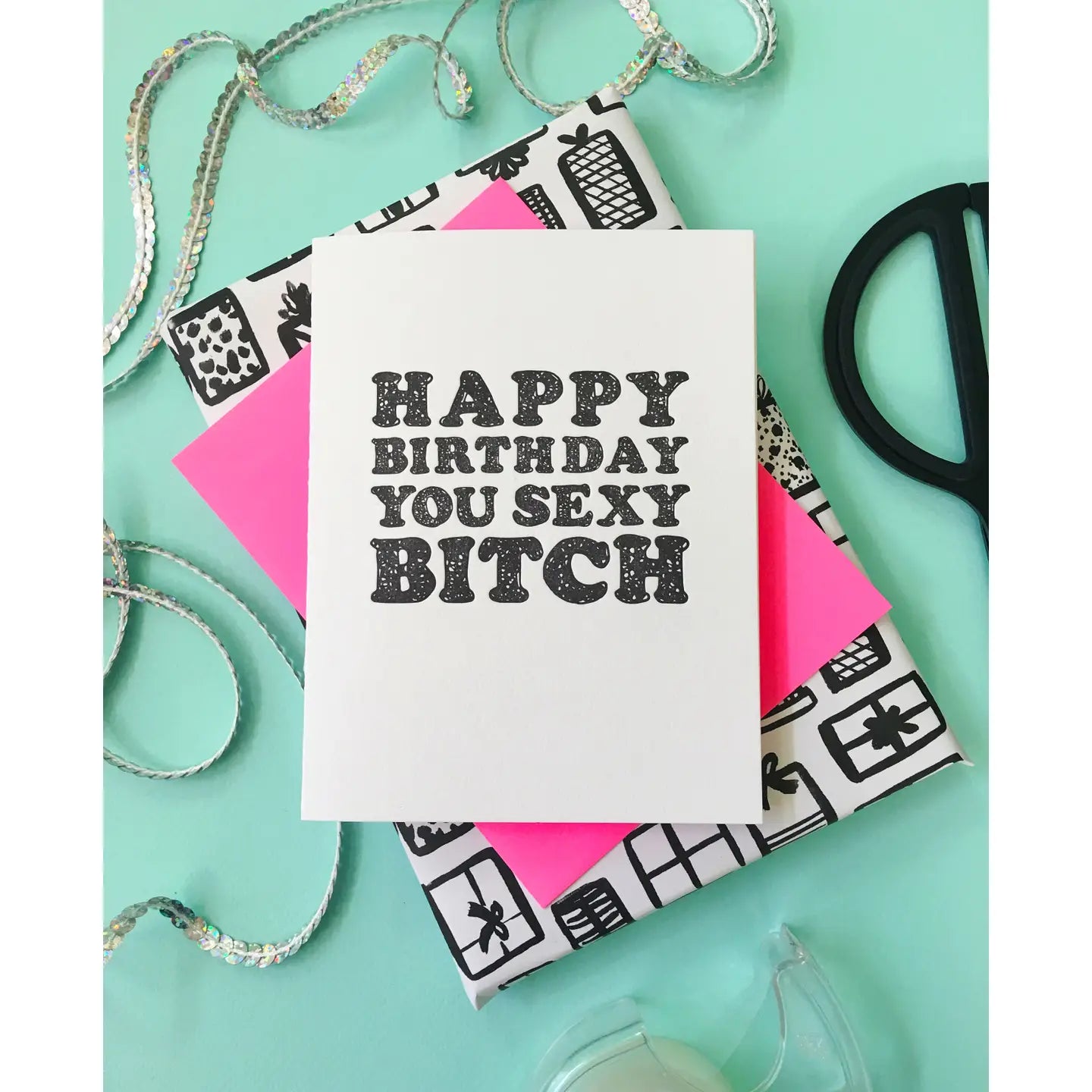 Card with 'Happy Birthday You Sexy Bitch' text on a decorative box with ribbons and scissors.