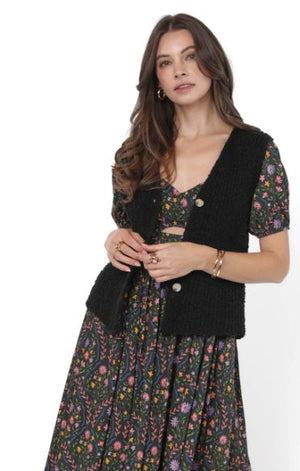 Woman wearing a black cardigan over a floral dress on a white background