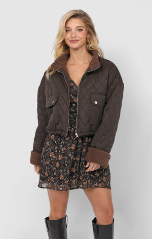 Woman wearing a brown quilted jacket over a floral dress on a white background