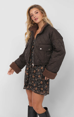 Woman wearing a brown quilted jacket over a floral dress on a white background