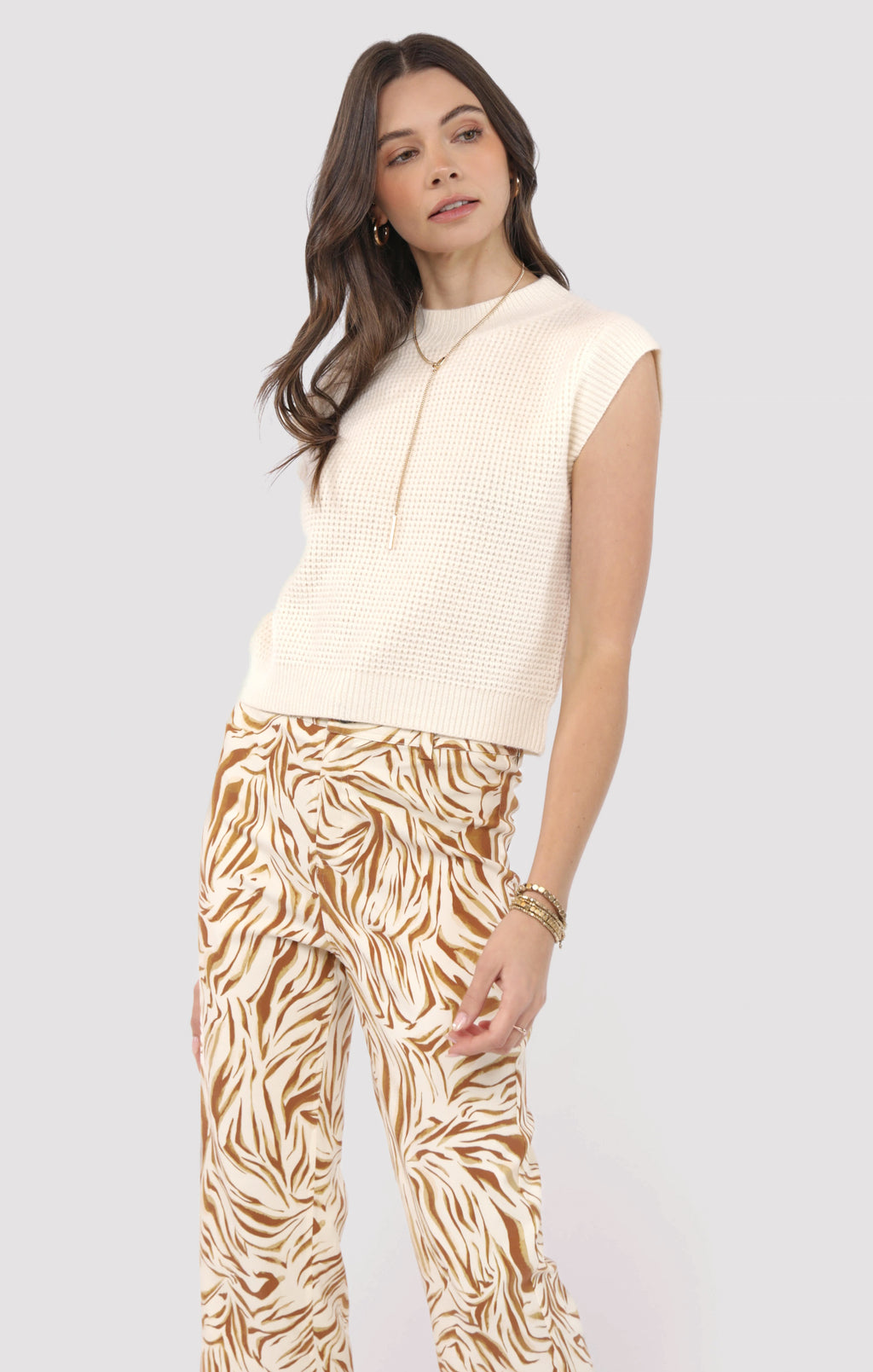 Woman wearing a sleeveless beige top and patterned pants on a light gray background
