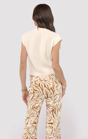 Woman wearing a cream top and patterned pants on a white background