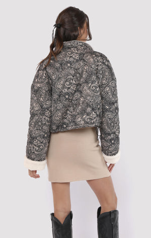 Person wearing a patterned jacket and beige skirt on a white background