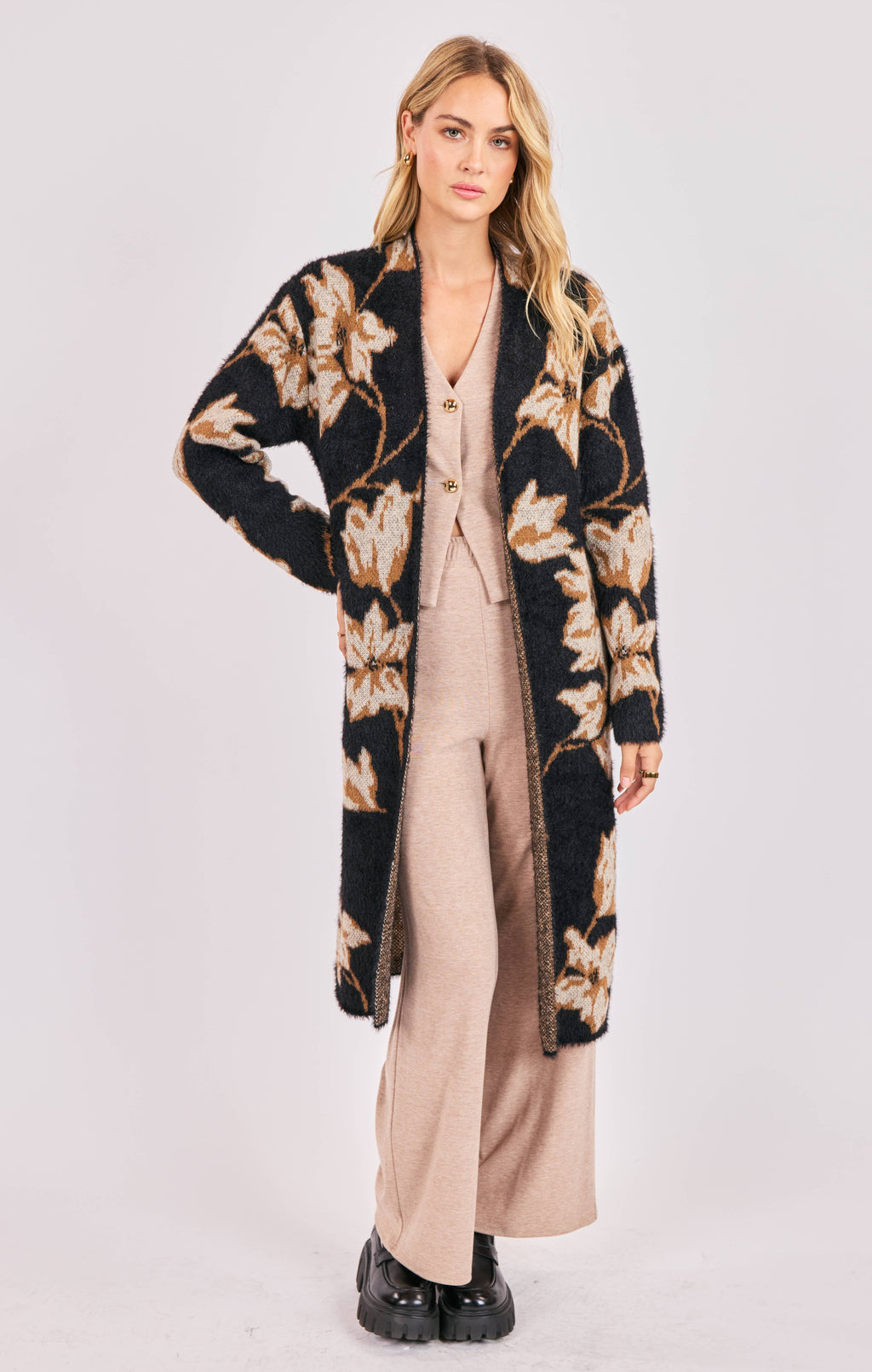 Woman wearing a long floral cardigan over a beige outfit on a white background