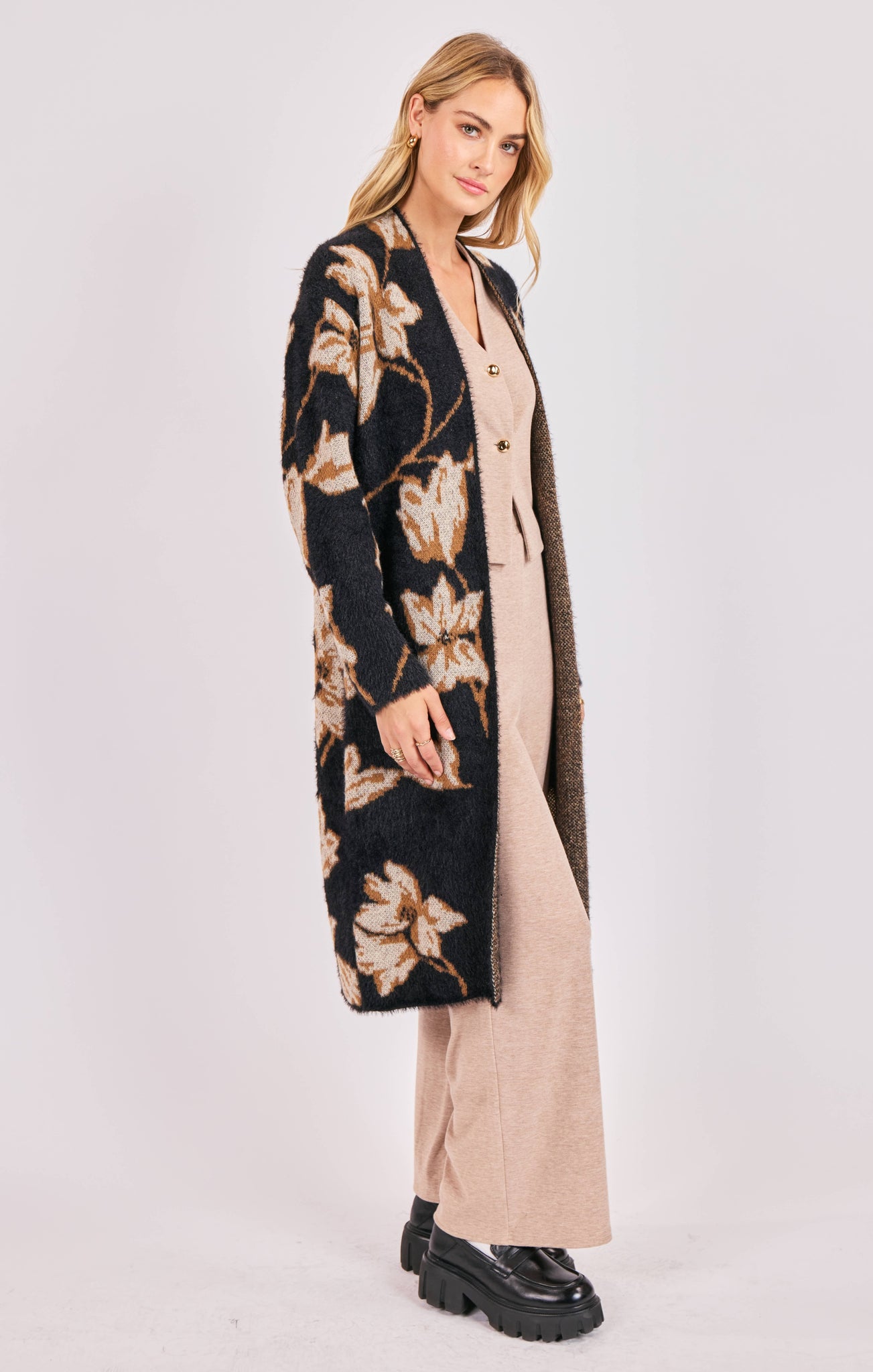 Woman wearing a long floral cardigan over a beige dress on a white background