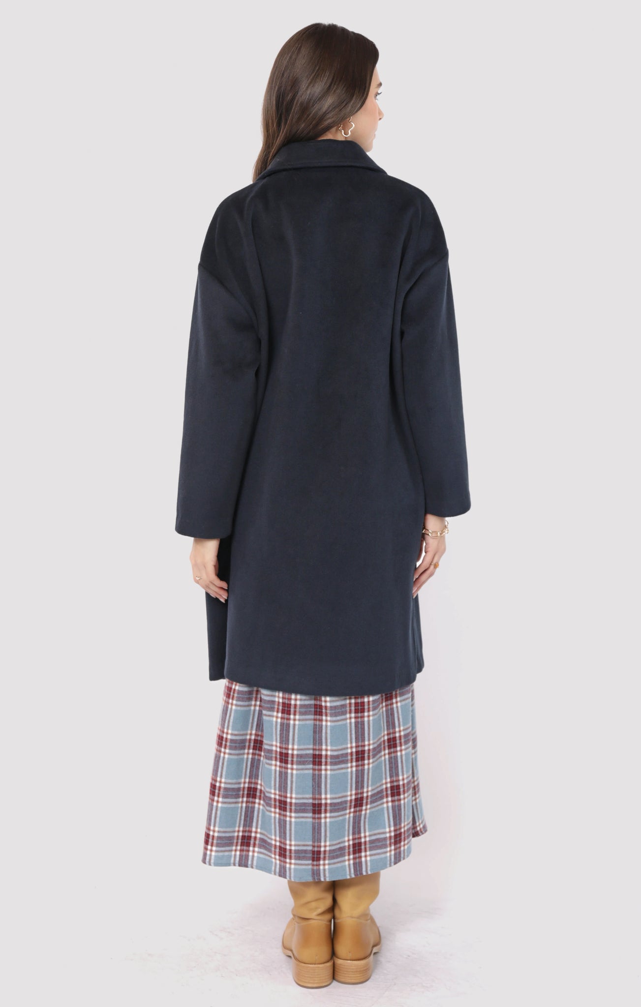 Woman wearing a long dark coat over a plaid skirt on a white background