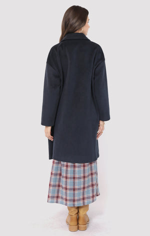 Woman wearing a long dark coat over a plaid skirt on a white background