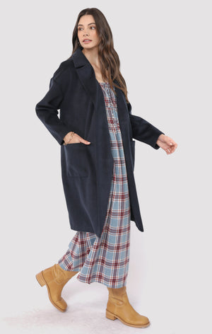 Woman wearing a long dark coat over a plaid dress with tan boots on a white background