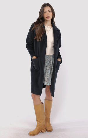 Woman wearing a black coat, beige sweater, patterned skirt, and tan boots on a white background