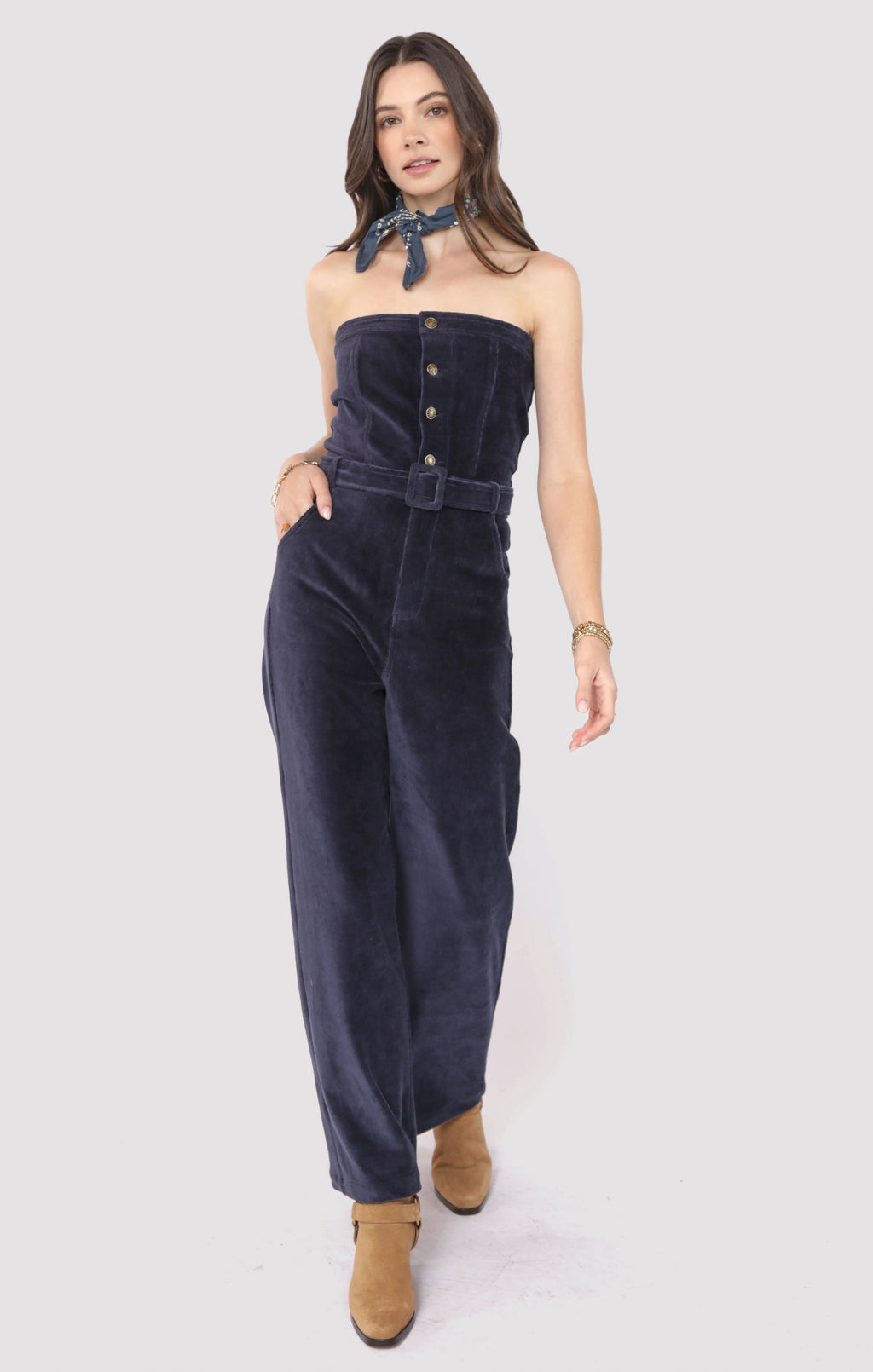 Woman wearing a navy velvet strapless jumpsuit on a white background
