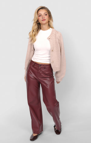 Woman wearing a pink cardigan, white top, and red pants on a light gray background