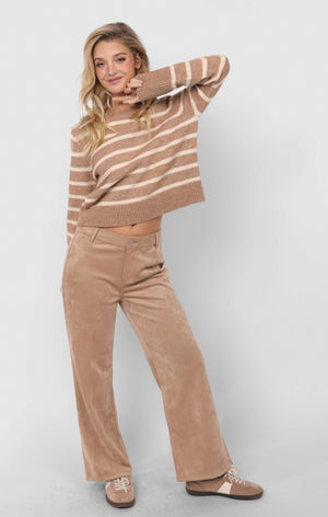 Woman wearing a brown and beige striped sweater and tan pants on a white background