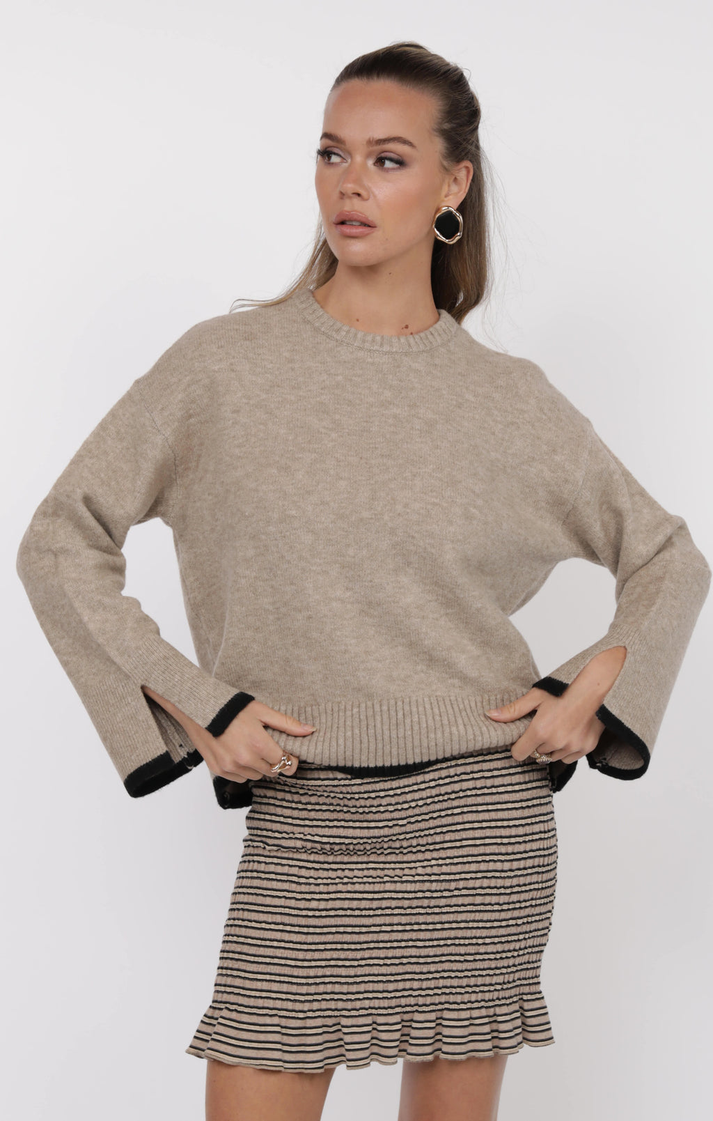 Woman wearing a beige sweater and striped skirt on a white background