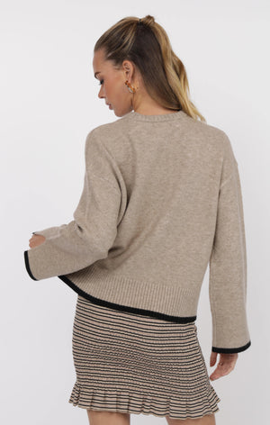 Woman wearing a beige sweater and striped skirt on a white background