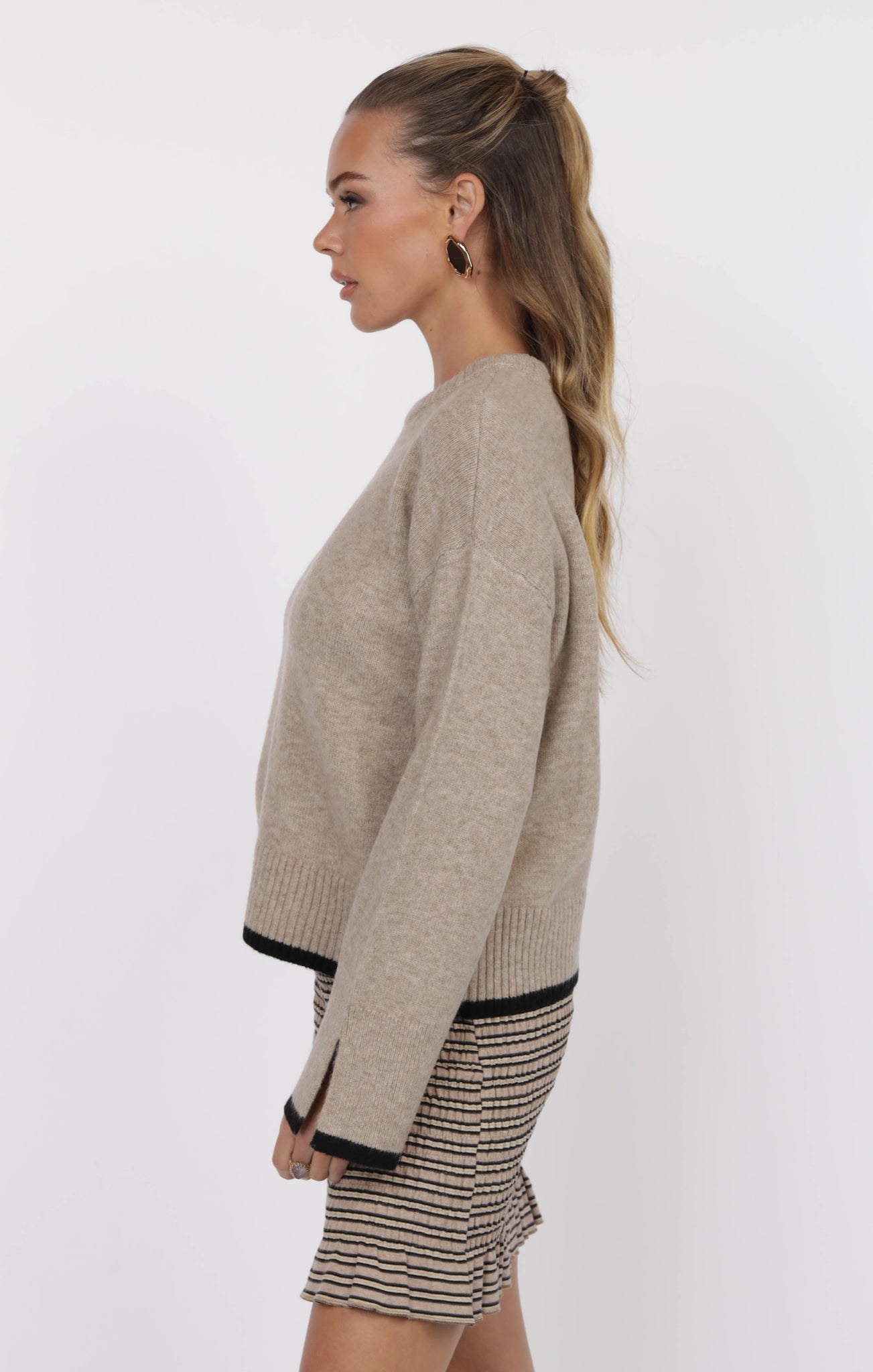 Woman wearing a beige sweater and striped skirt on a white background