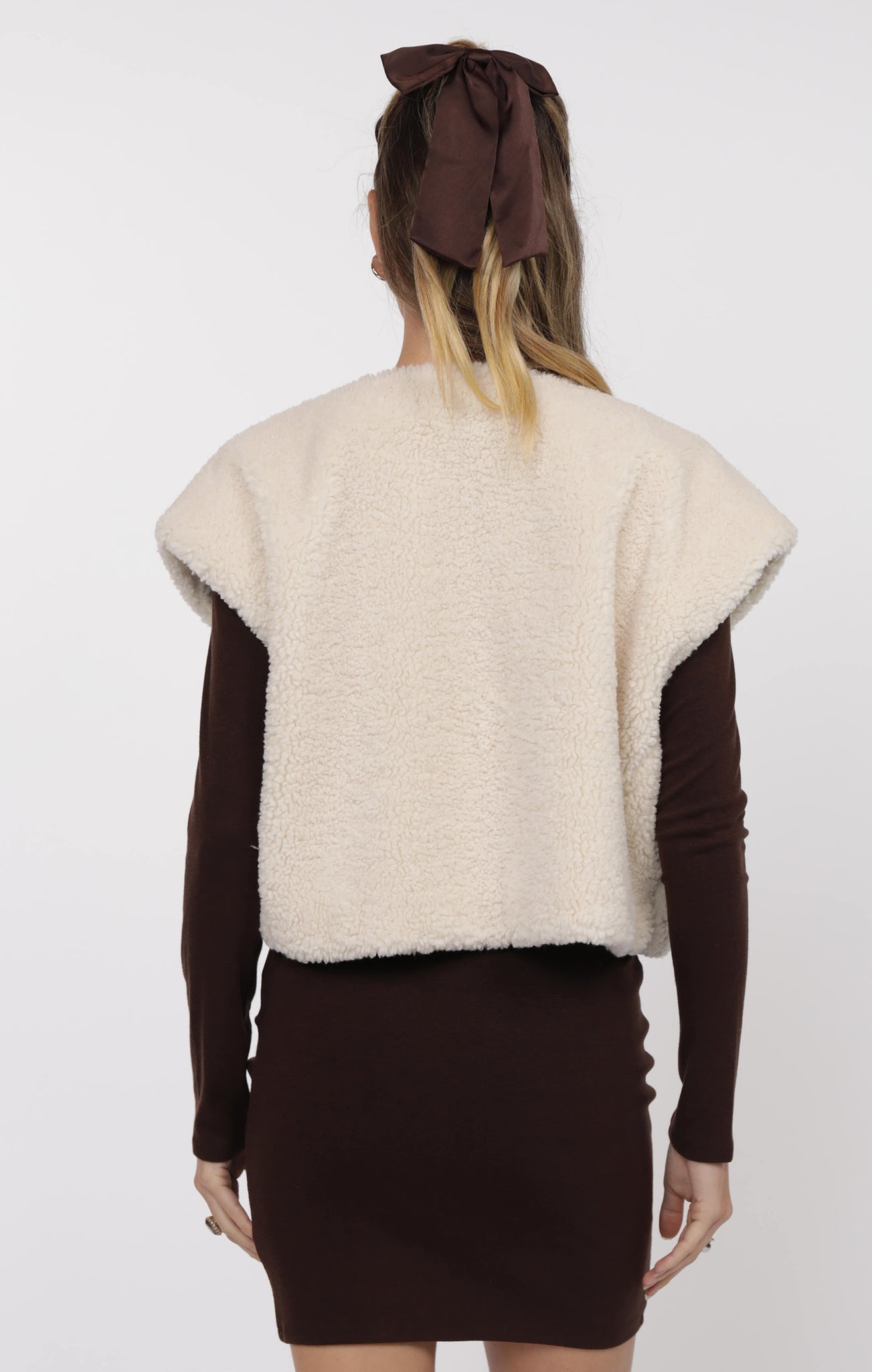 Person wearing a cream sweater vest over a brown dress with a brown headband on a white background
