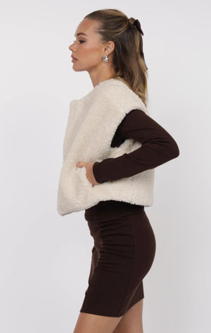 Woman wearing a white fleece vest over a brown outfit on a white background
