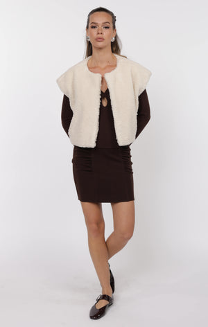 Woman wearing a white fur vest over a black outfit on a white background