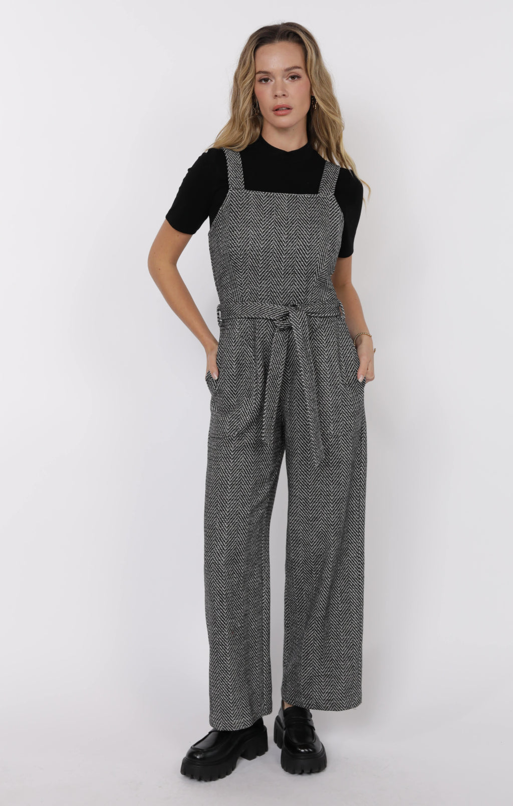 Woman wearing a gray houndstooth patterned jumpsuit on a white background
