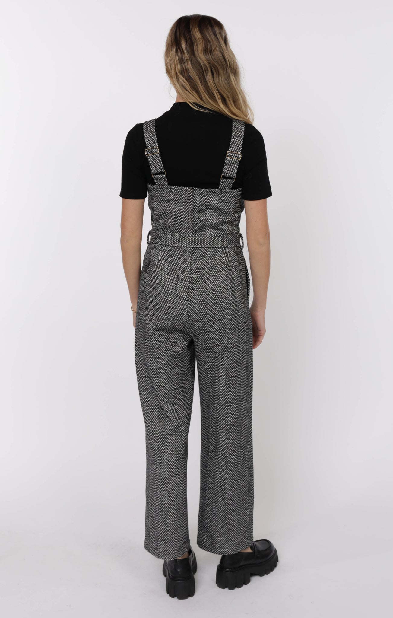 Person wearing a black top and gray checkered overalls on a white background