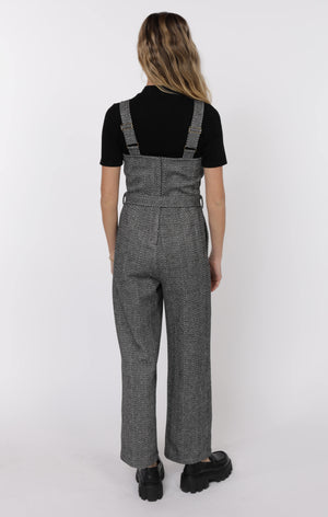 Person wearing a black top and gray checkered overalls on a white background