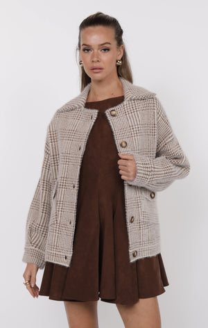 Woman wearing a plaid coat over a brown dress on a white background