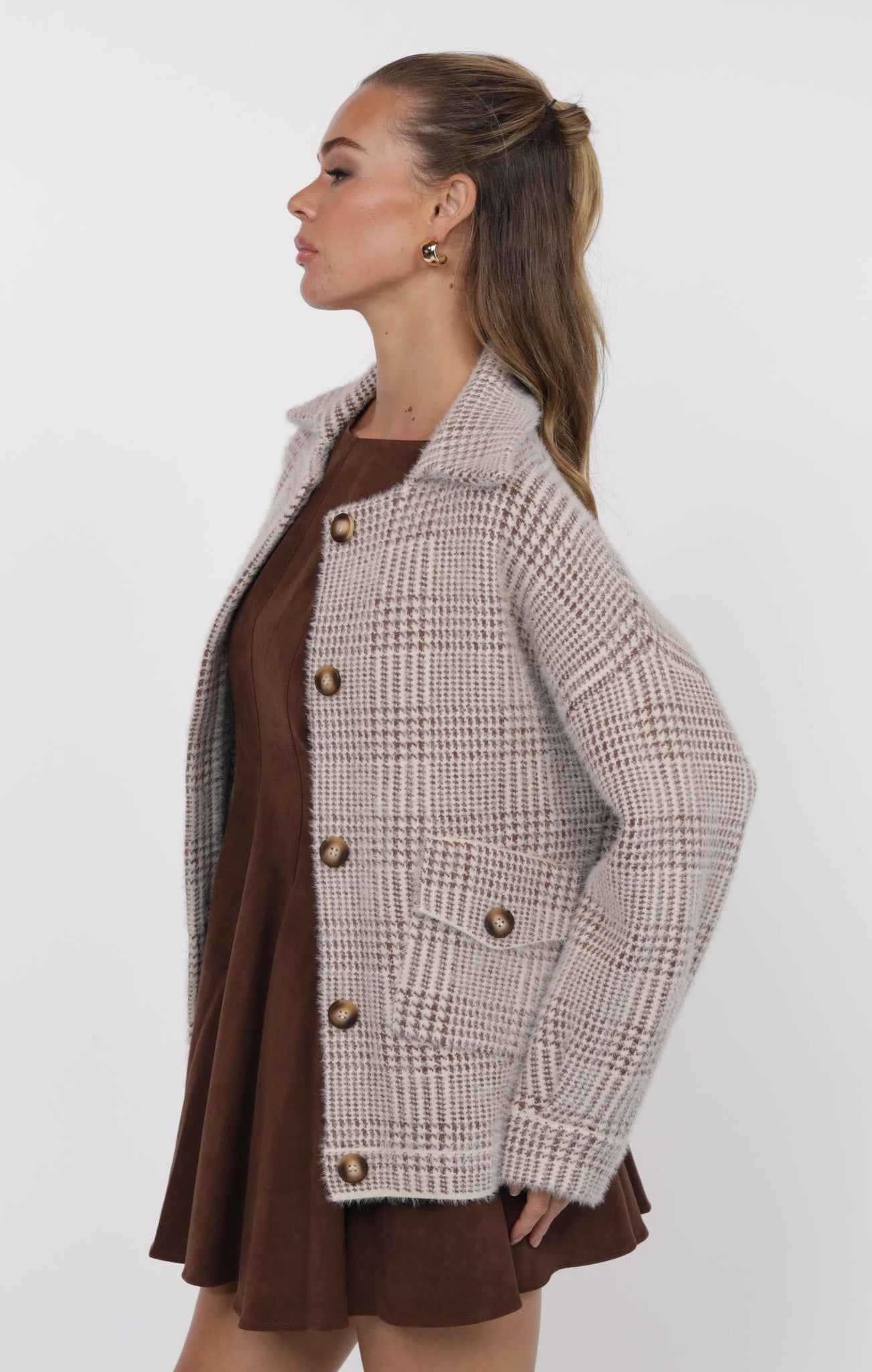 Woman wearing a plaid coat over a brown dress on a white background