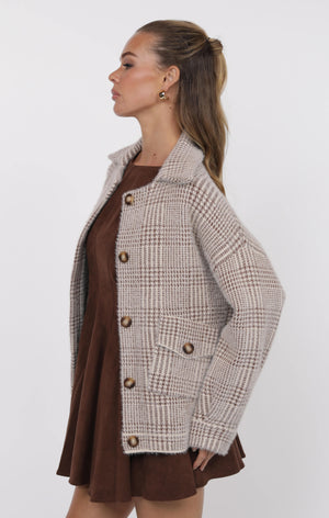 Woman wearing a plaid coat over a brown dress on a white background