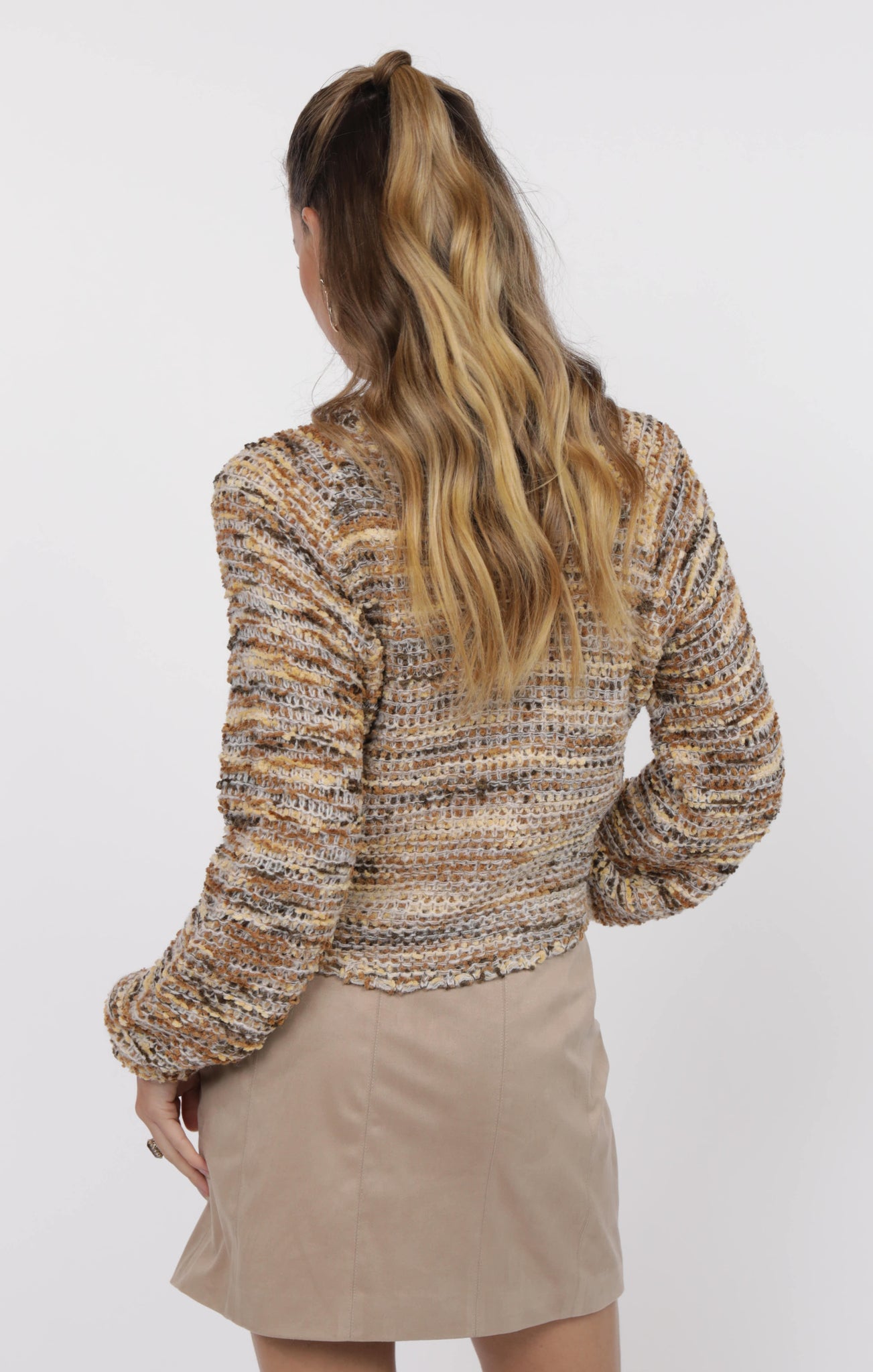 Person wearing a patterned sweater and beige skirt on a white background