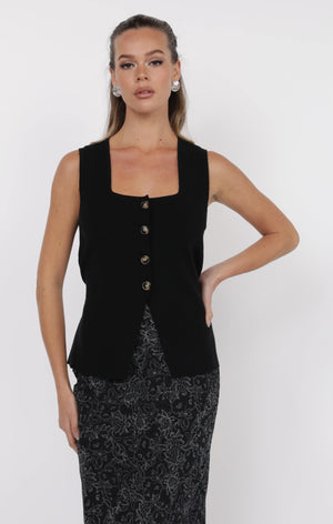 Woman wearing a black sleeveless blazer over a patterned dress on a white background