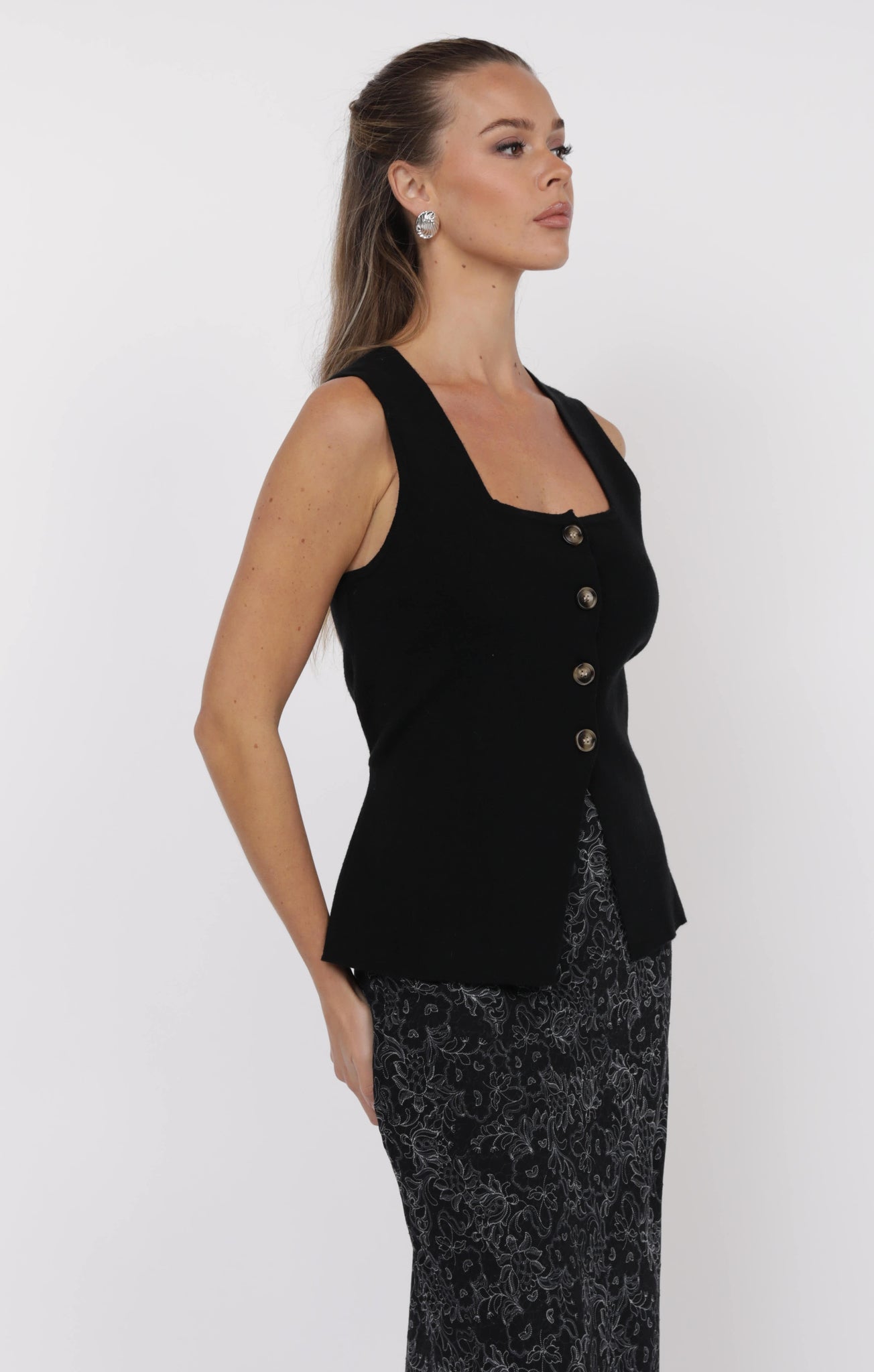 Woman wearing a black sleeveless top with buttons on a white background