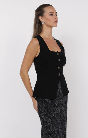 Woman wearing a black sleeveless top with buttons on a white background