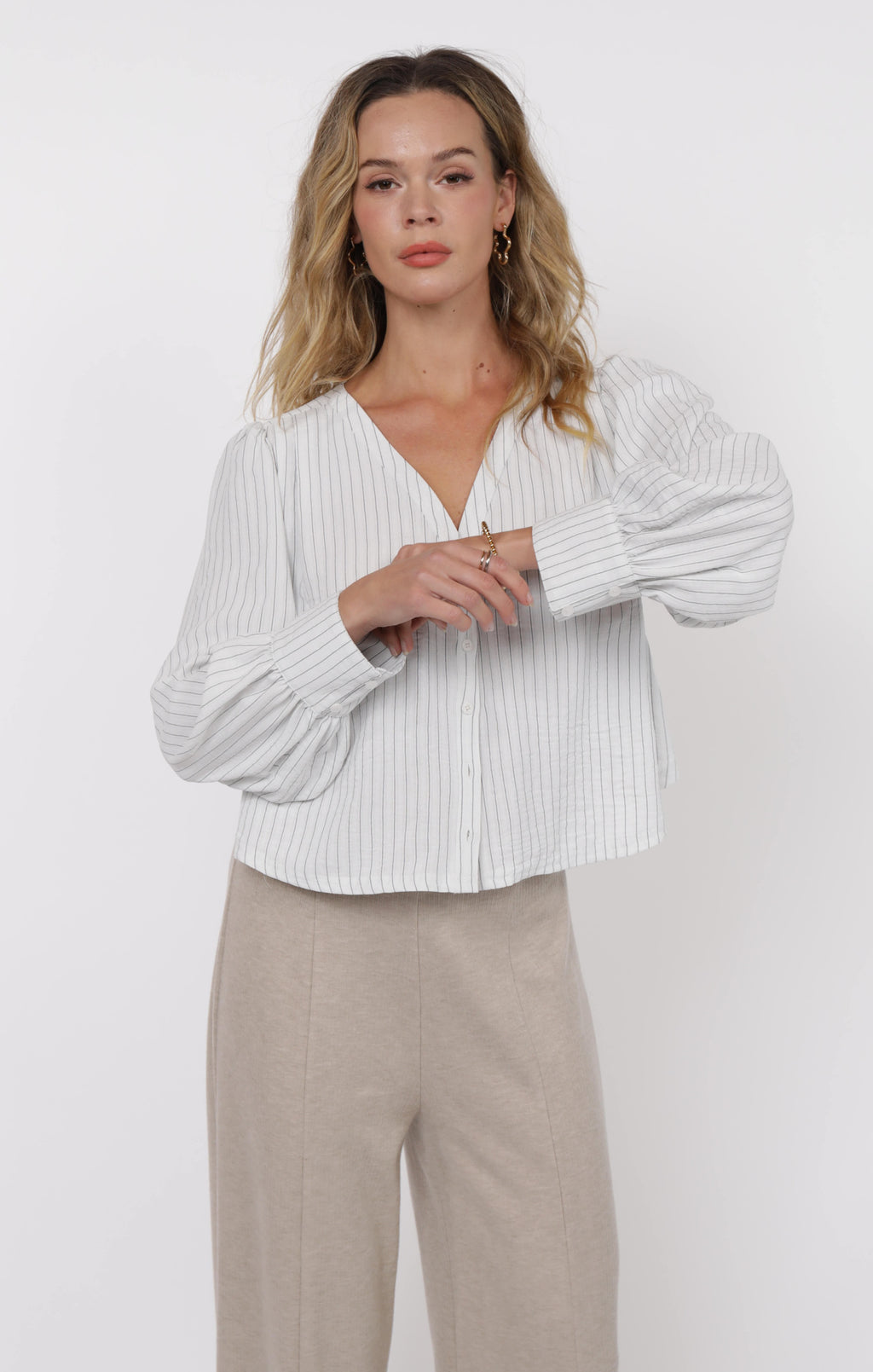 Woman wearing a white ribbed blouse and beige pants on a white background